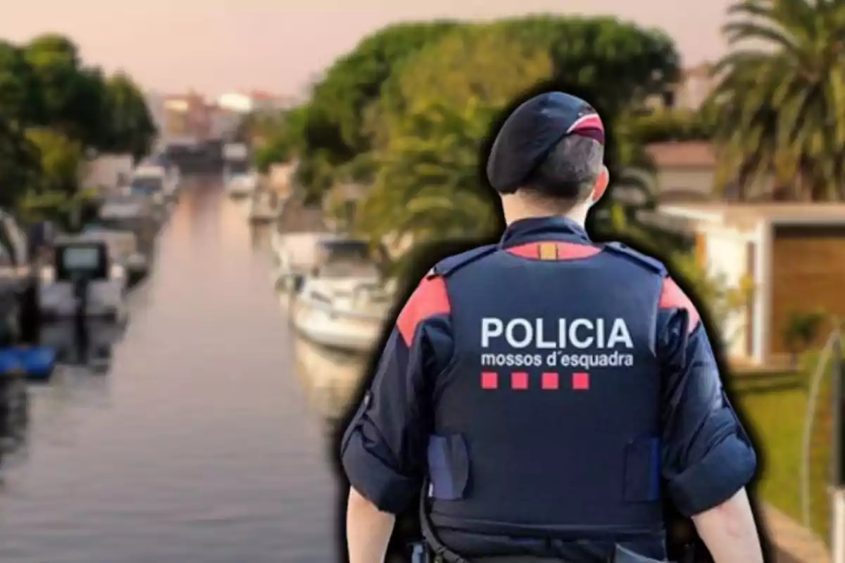 Un agent dels Mossos d'Esquadra d'esquena davant d'un canal amb vaixells i vegetació.