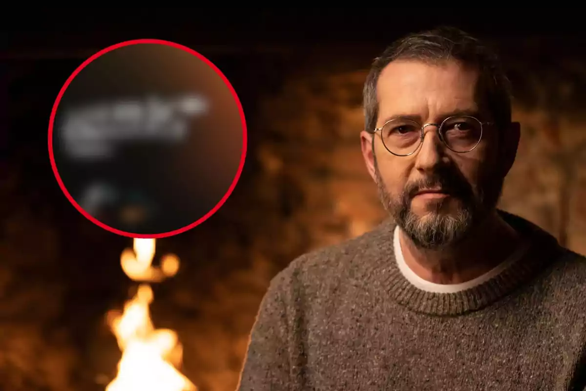 Hombre con gafas y barba frente a una chimenea con un círculo rojo desenfocado en el fondo.