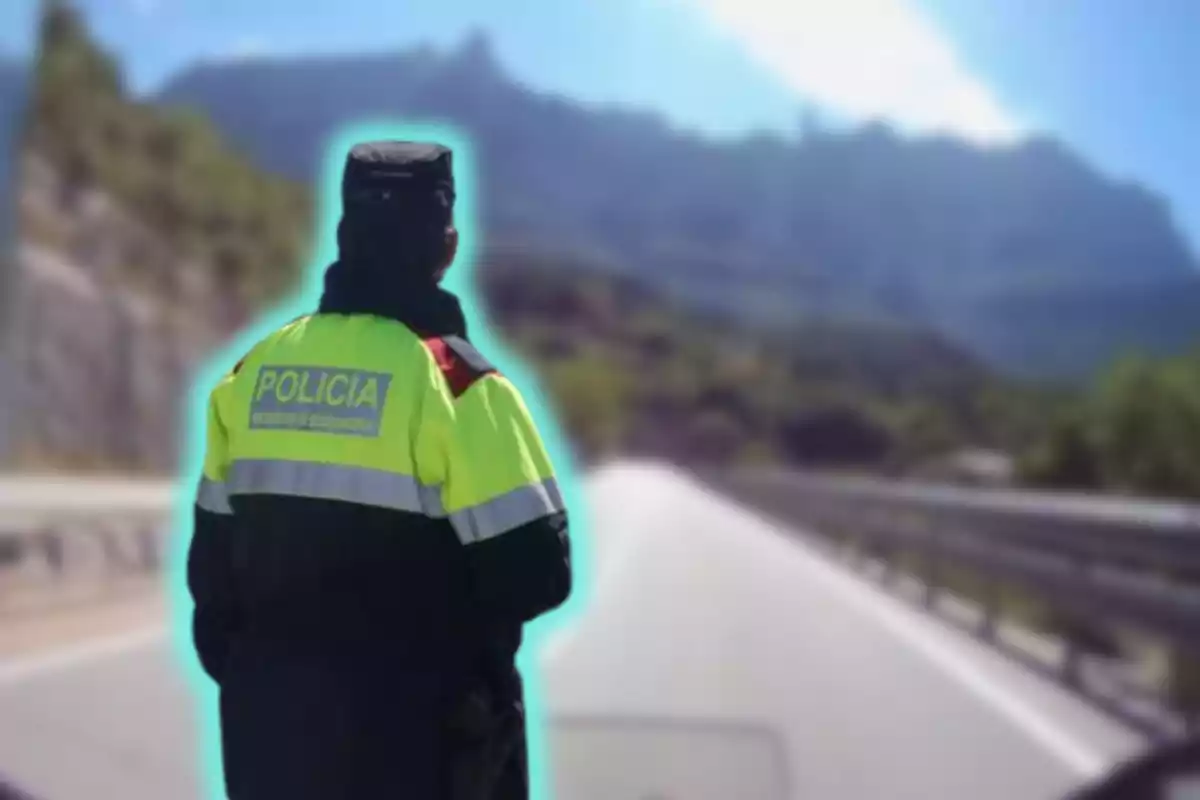 Un policia amb uniforme groc i negre d?esquena en una carretera amb muntanyes al fons.