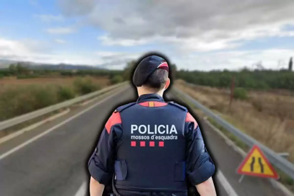 Un agente de policía de espaldas en una carretera con un paisaje rural y una señal de tráfico a un lado.