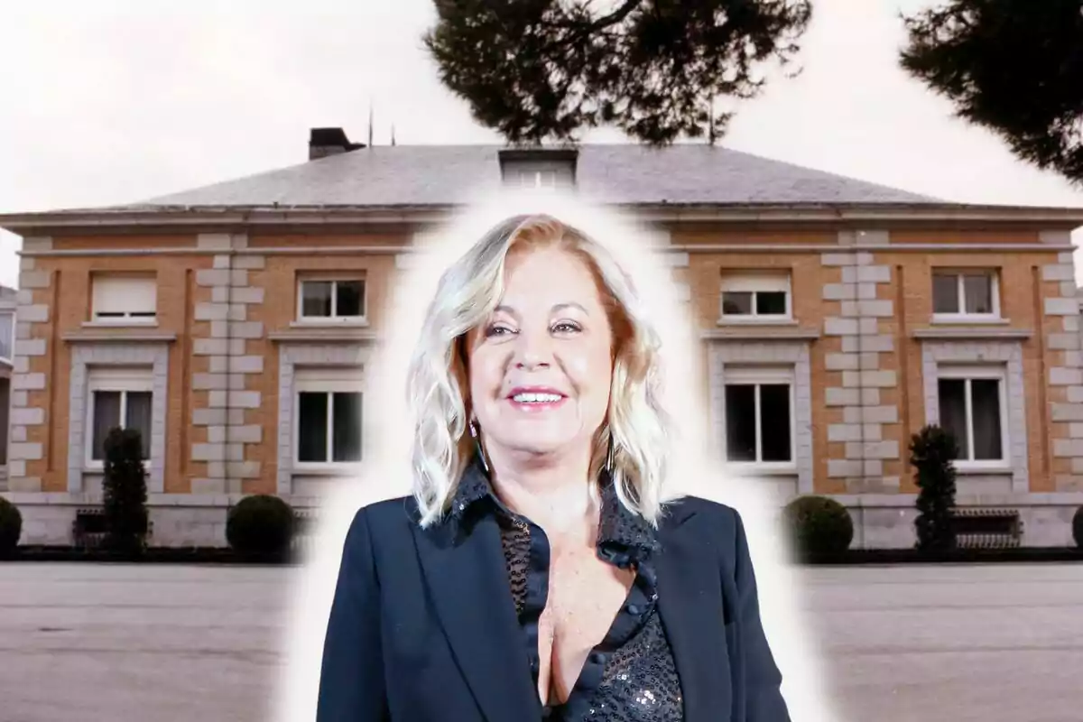 Una mujer sonriente con cabello rubio y chaqueta oscura frente a un edificio de ladrillo con ventanas blancas.