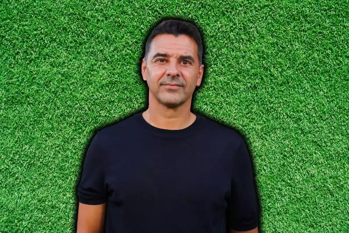 Hombre con camiseta negra posando frente a un fondo de césped verde.