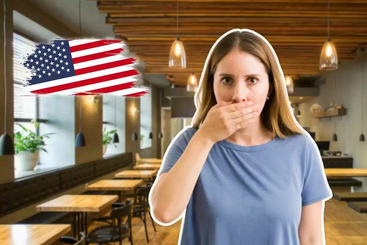 Dona sorpresa cobrint-se la boca amb una mà en un restaurant modern amb una bandera dels Estats Units pintada al fons