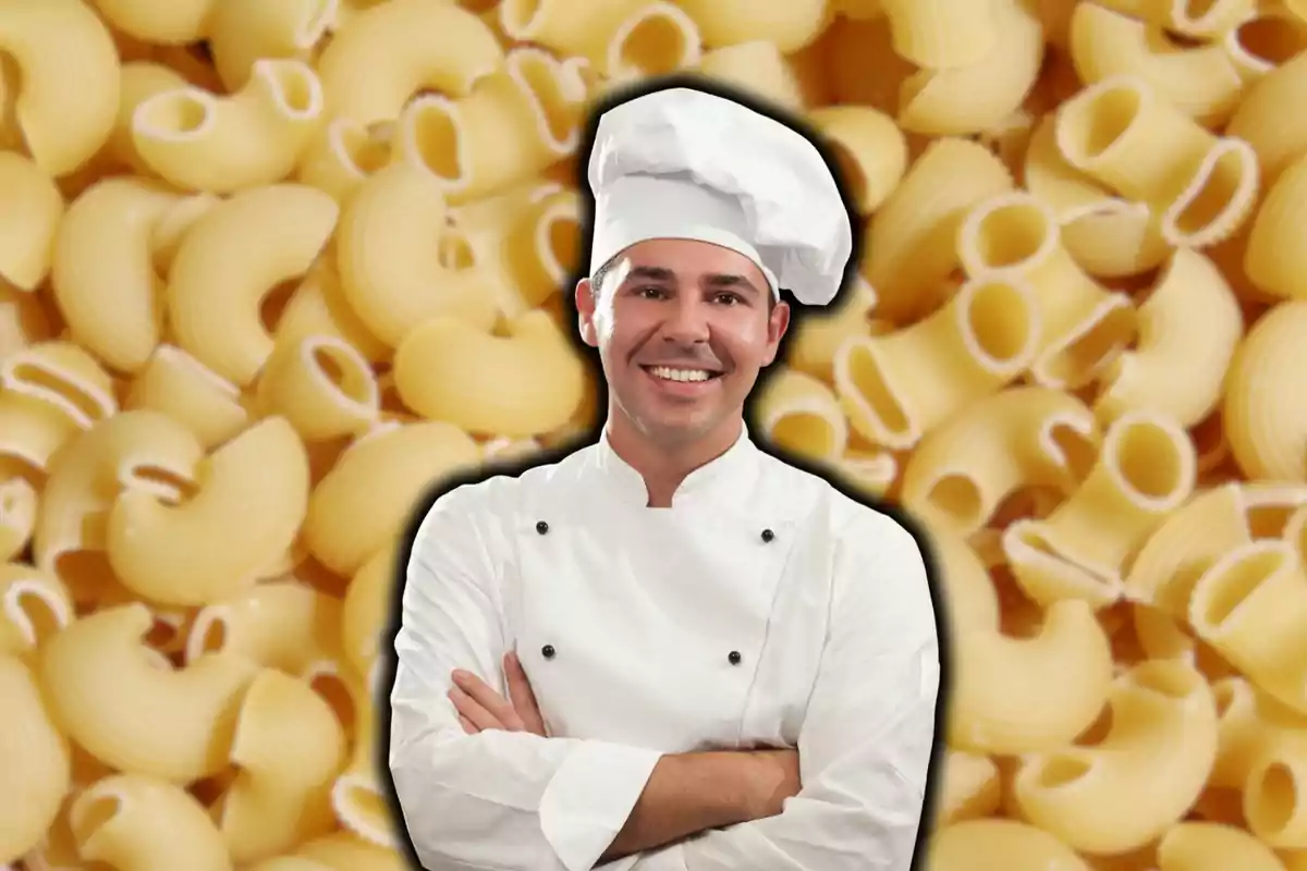 Un xef somrient amb uniforme blanc i gorra de cuiner davant d'un fons de pasta.