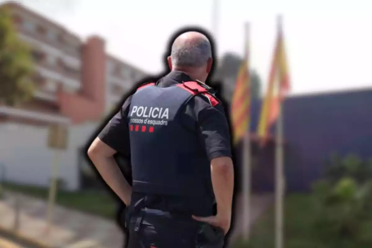 Un agent de policia d?esquena amb uniforme dels Mossos d?Esquadra en un entorn urbà amb banderes al fons.