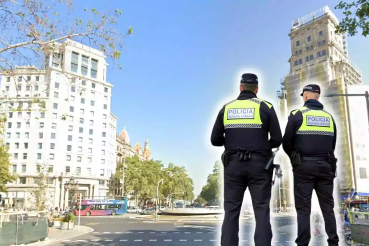 Dos agents de la Guàrdia Urbana d'esquena observen una intersecció en una ciutat amb edificis alts i un autobús de colors al fons.