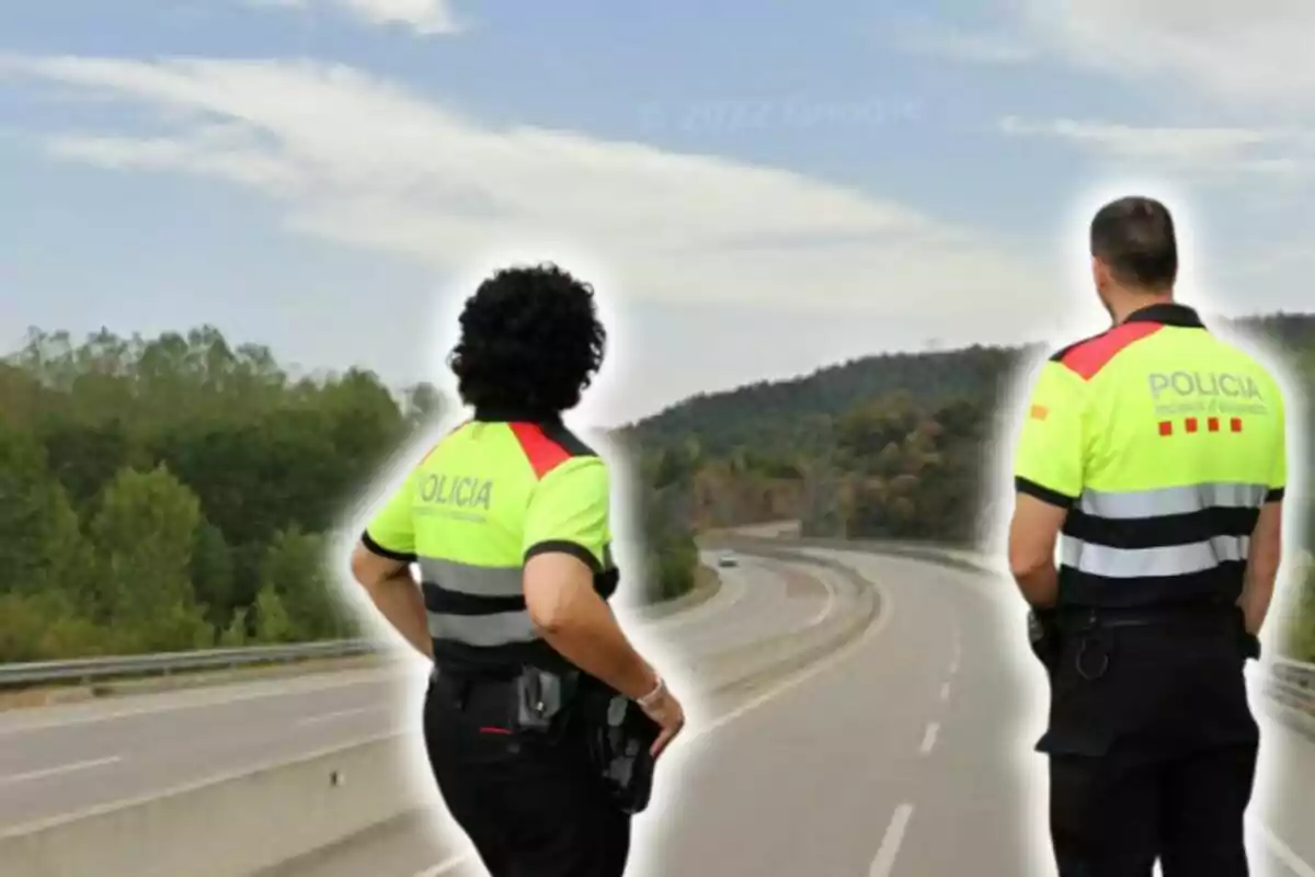 Dos agentes de policía de espaldas observando una carretera vacía.