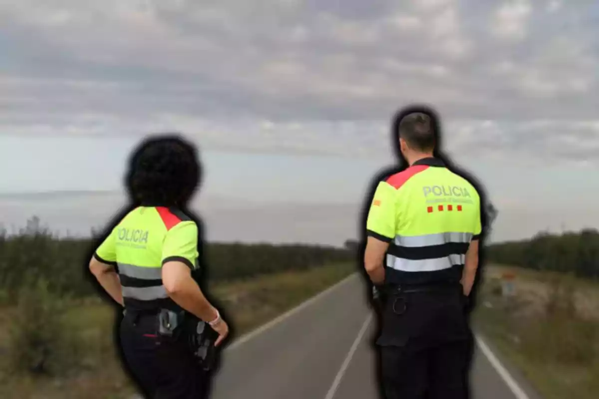 Dos agentes de policía con chalecos reflectantes observan una carretera desierta bajo un cielo nublado.