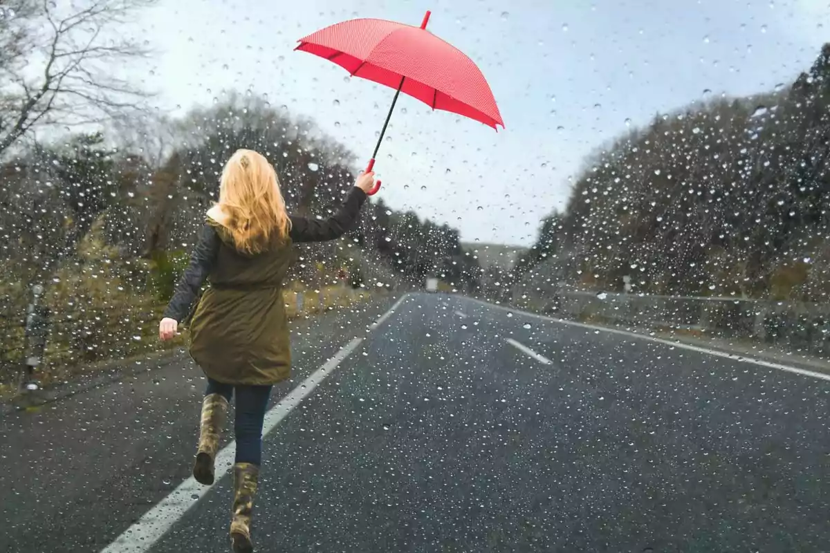 Persona caminant sota la pluja en una carretera amb un paraigua vermell.