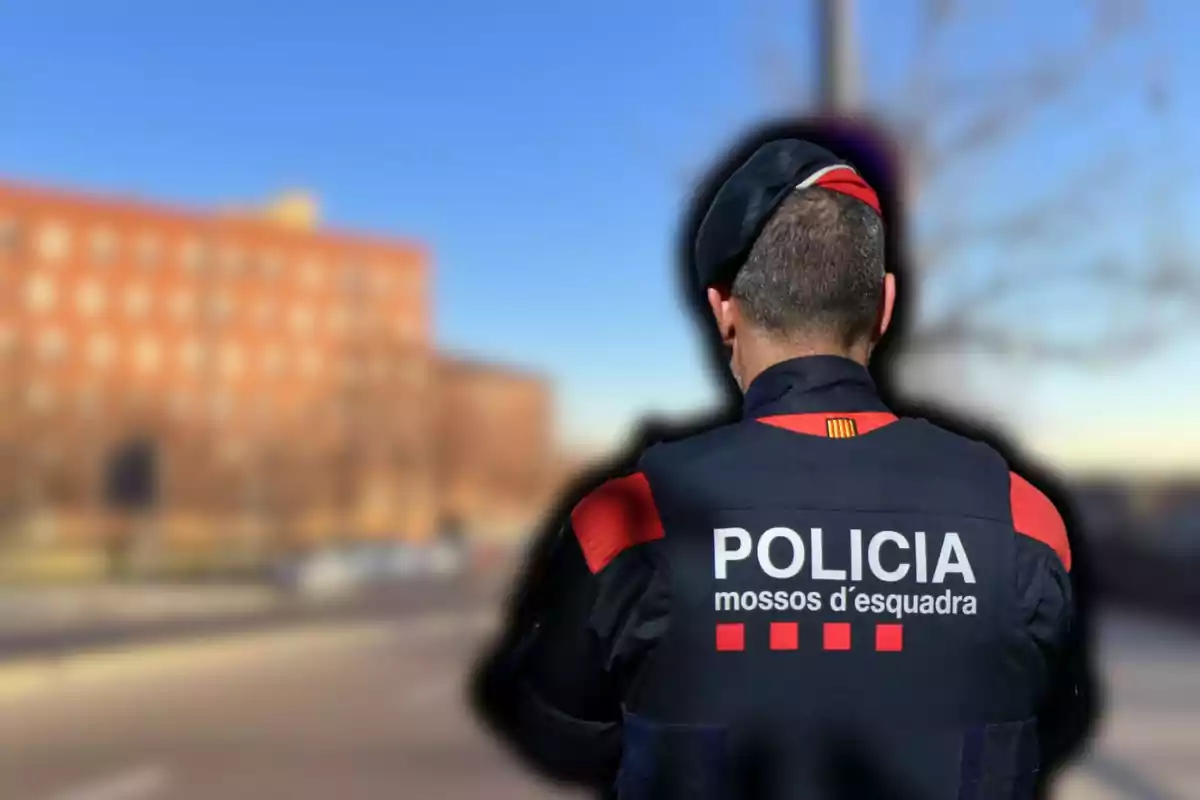 Un agent dels Mossos d'Esquadra d'esquena a un carrer amb un edifici de fons.