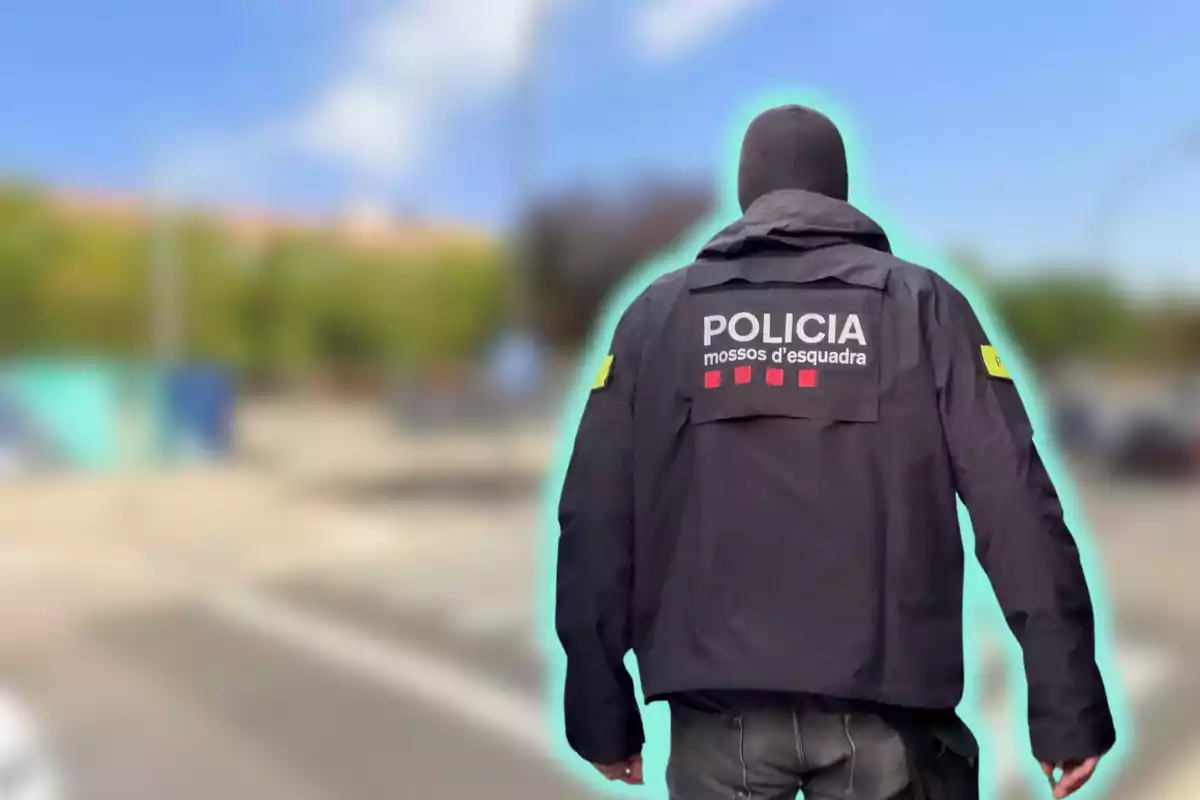 Policia dels Mossos d'Esquadra d'esquena amb uniforme negre en un entorn urbà desenfocat.