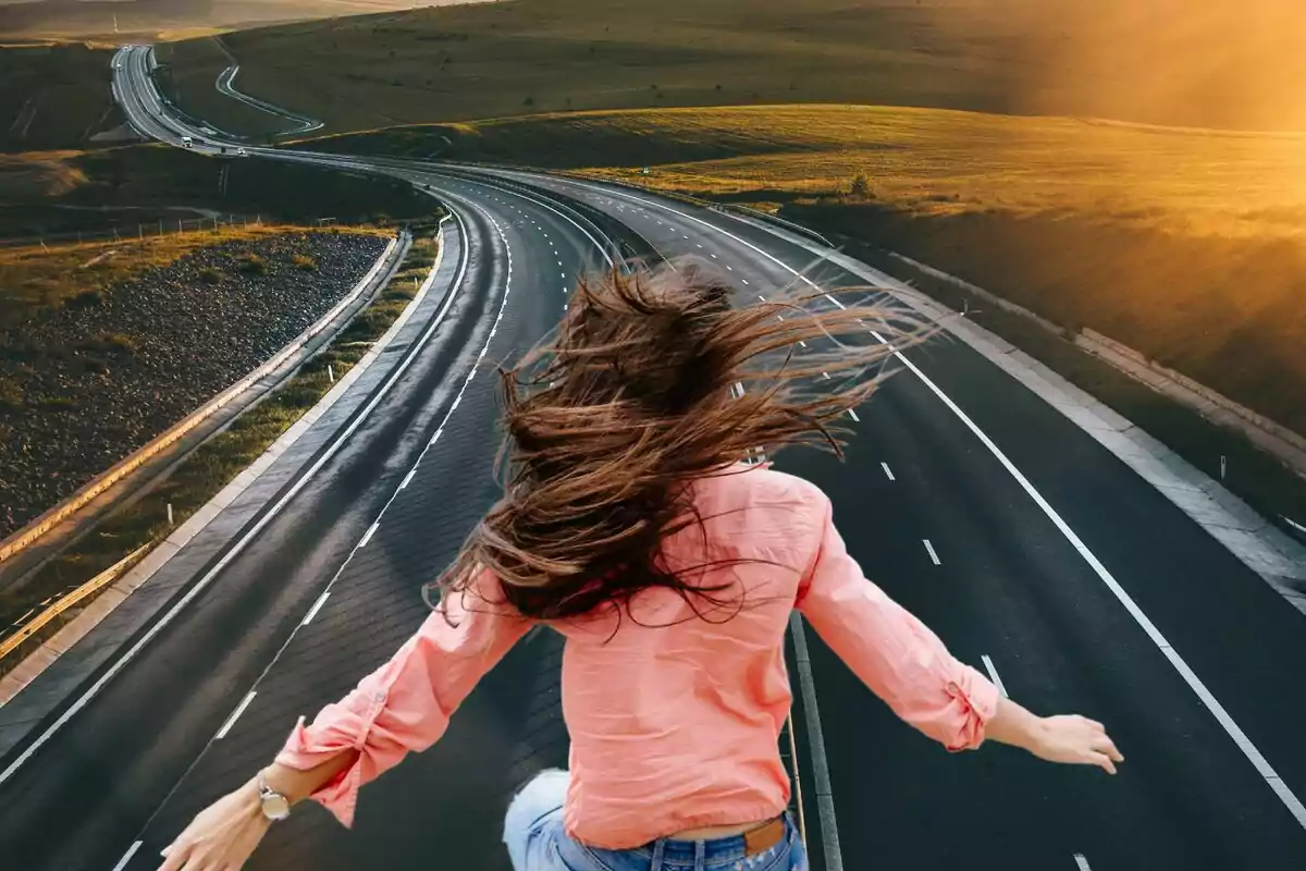 Persona con cabello largo y suelto de espaldas en una carretera vacía al atardecer