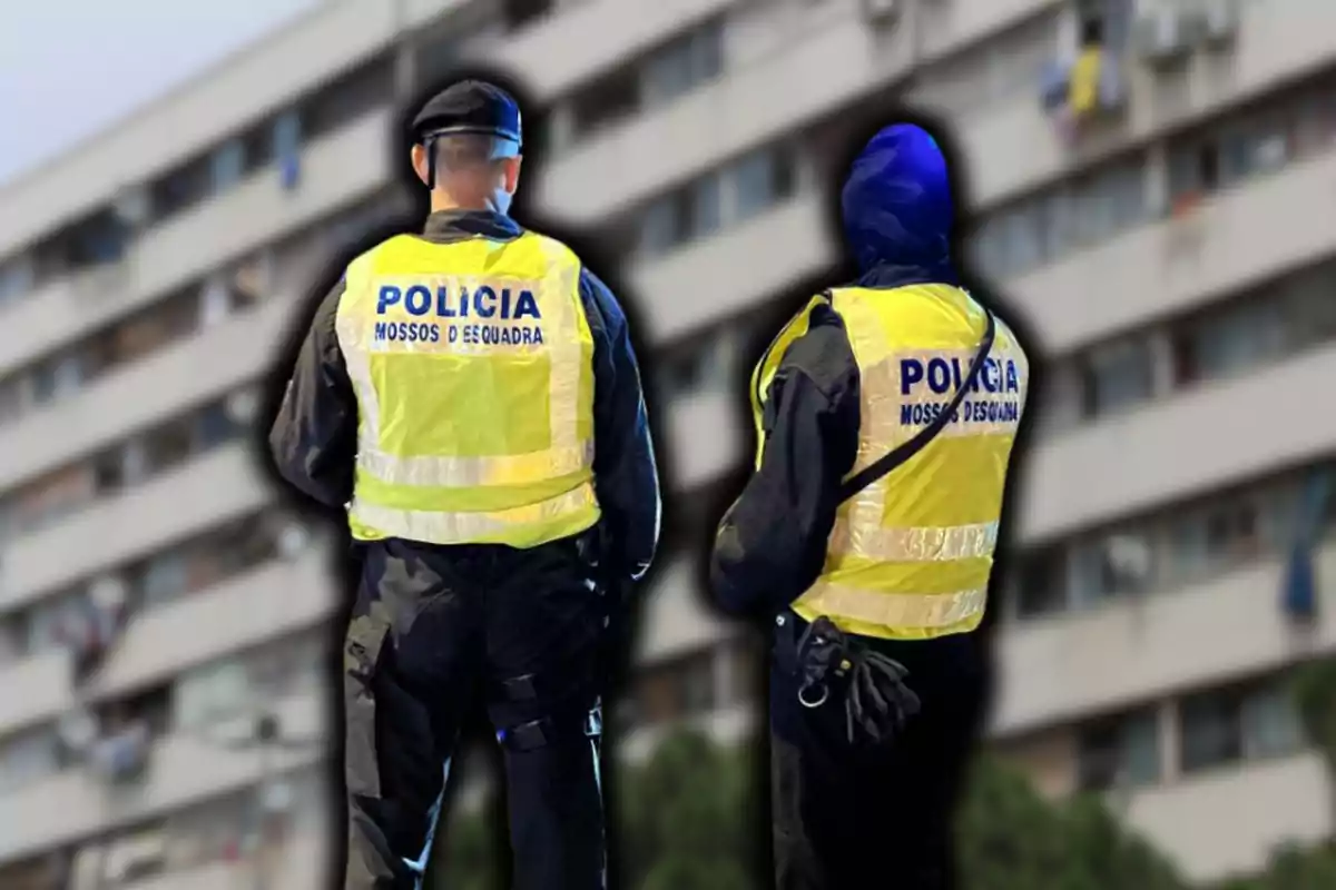 Dos agents de policia amb armilles reflectores dels Mossos d'Esquadra d'esquena davant d'un edifici residencial.