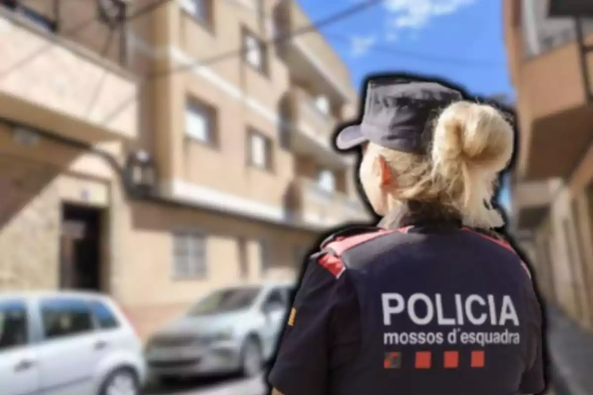 Una agent de policia dels Mossos d'Esquadra d'esquena a un carrer amb edificis i cotxes estacionats.