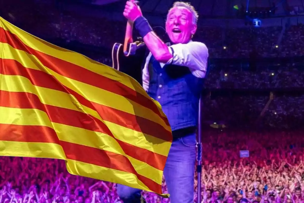 Un músico en el escenario sosteniendo una guitarra con una bandera catalana ondeando en primer plano y una multitud de fondo.