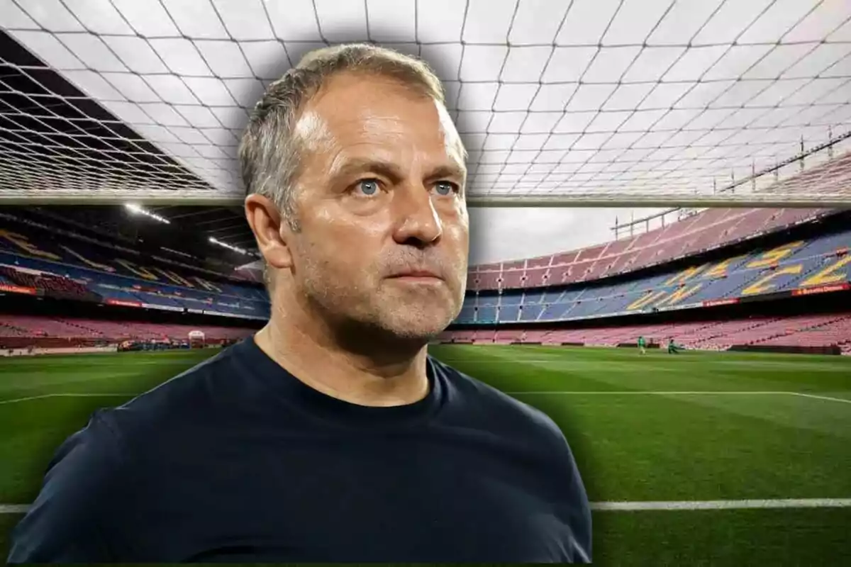 Un homme aux cheveux gris courts et à l’expression sérieuse se tient devant un stade de football vide.