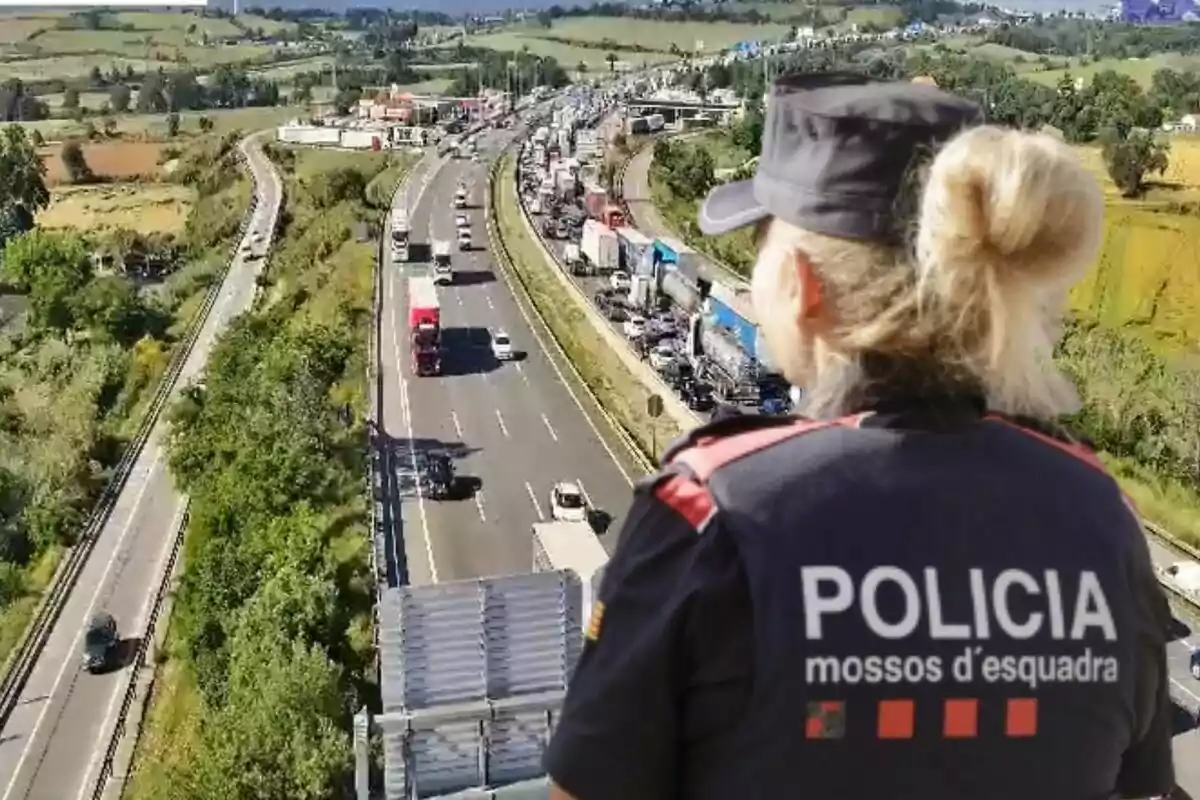 Una agente de policía observa una autopista con tráfico denso desde un punto elevado, rodeada de un paisaje verde y rural.
