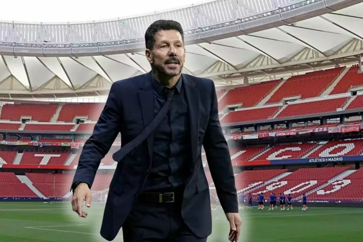 Un hombre con traje oscuro camina en un estadio de fútbol vacío con asientos rojos.