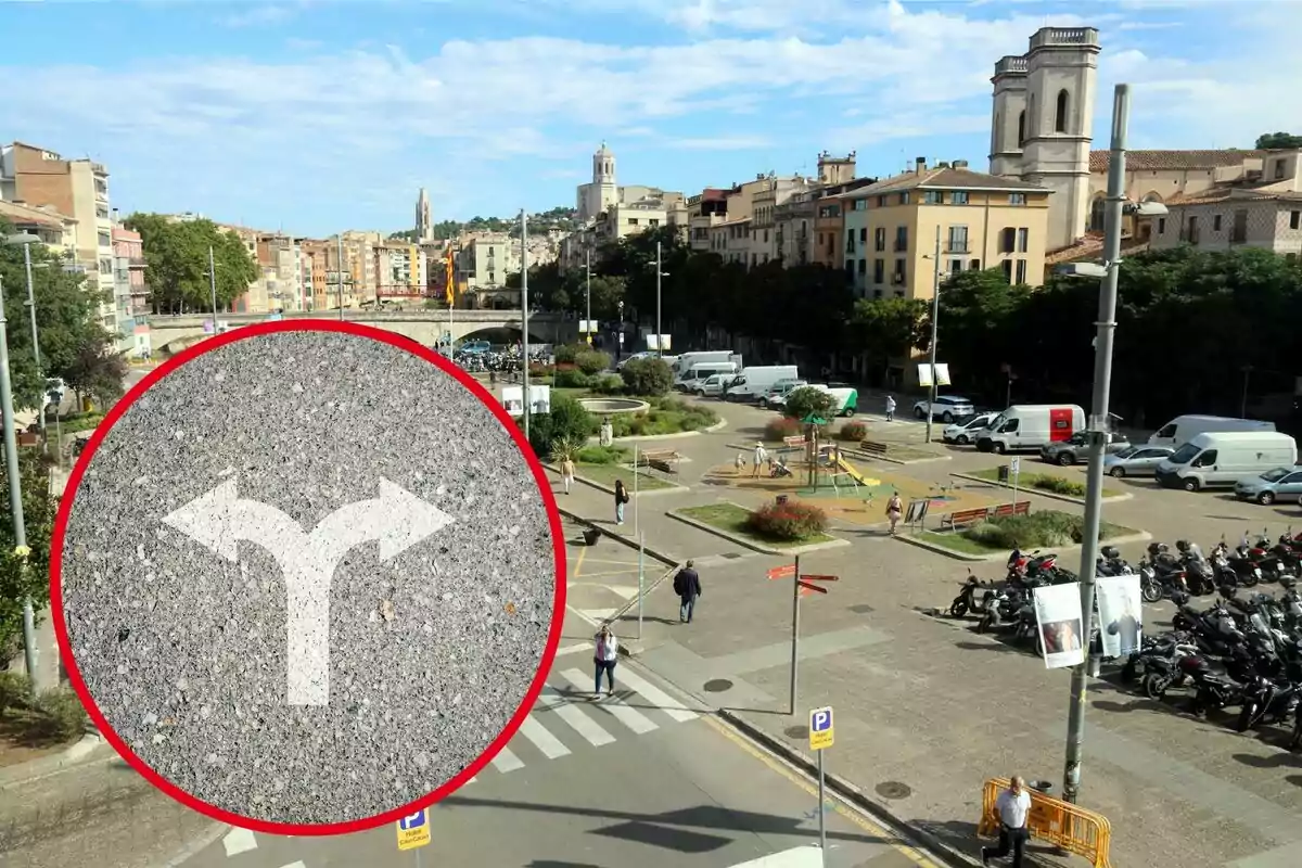 Vista aèria d'una plaça urbana amb parc infantil, estacionament de motocicletes i diversos edificis al fons, amb un cercle vermell que conté un senyal de trànsit indicant una bifurcació.