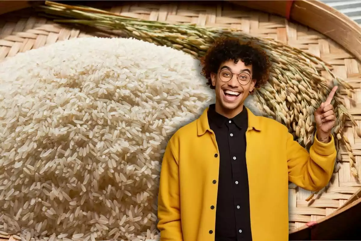 Una persona sonriente con gafas y chaqueta amarilla señala hacia un montón de arroz en un recipiente de mimbre.