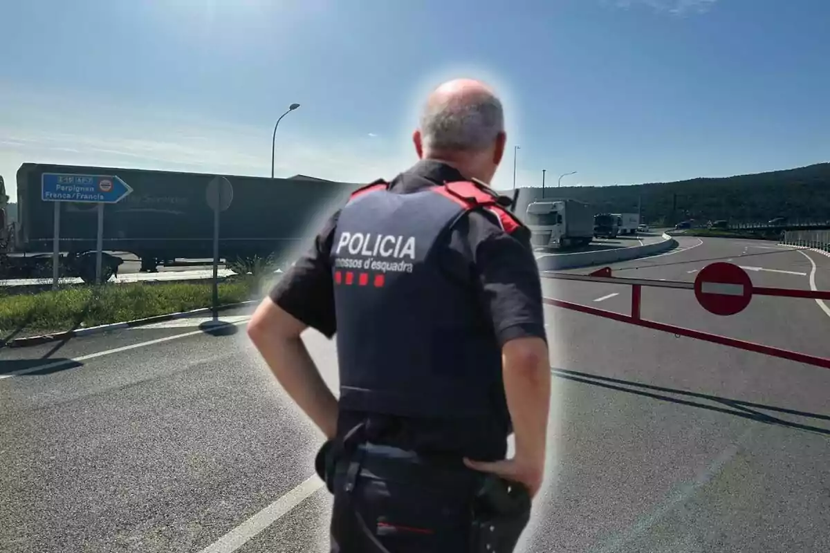 Un agent de policia d?esquena observa una carretera bloquejada amb un senyal de prohibit el pas i un cartell que indica la direcció cap a Perpinyà, França.