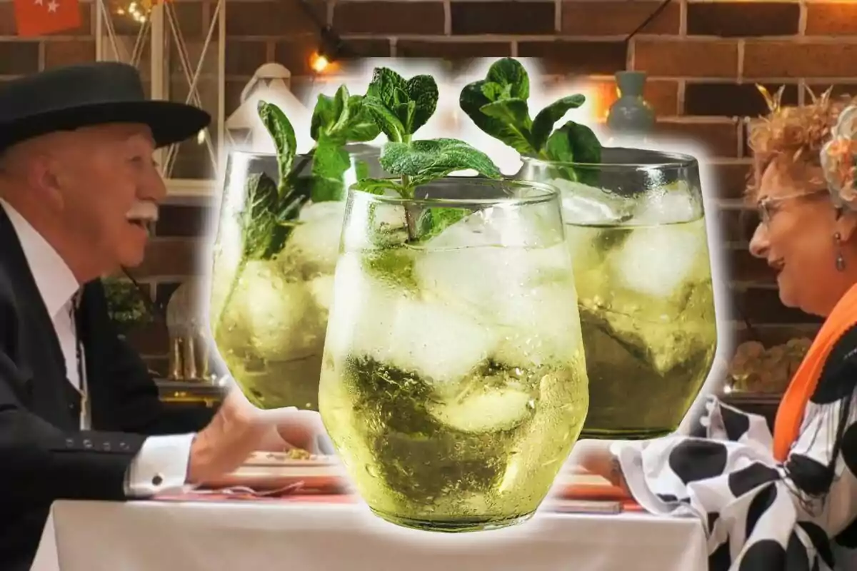 Una parella gran somriu mentre està asseguda en una taula, amb tres copes de còctel amb gel i menta en primer pla.