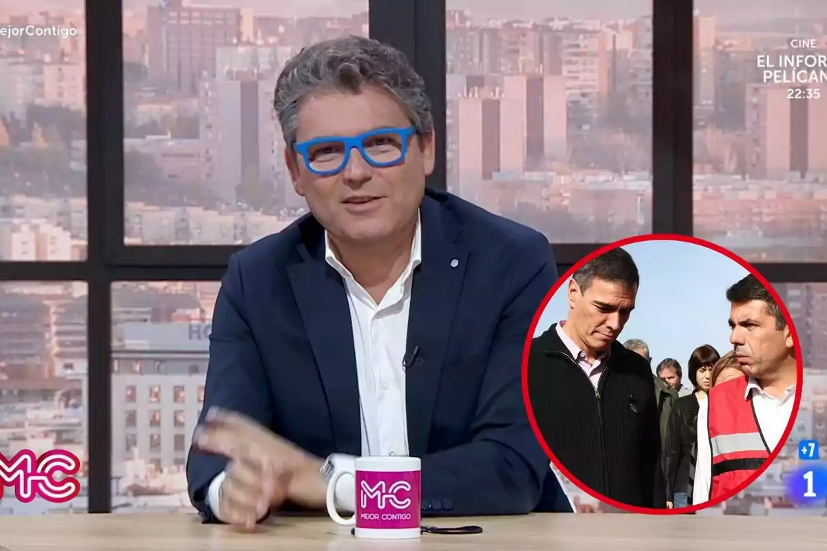 Un presentador de televisión con gafas azules está sentado en un estudio con una ventana de fondo y una taza con el logo "Mejor Contigo" sobre la mesa; en la esquina inferior derecha hay un recuadro con dos personas conversando al aire libre.