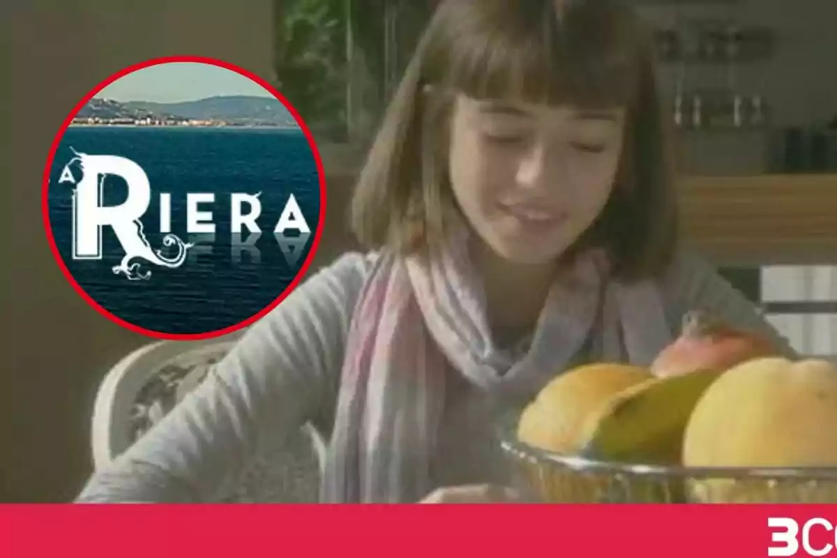 Una joven con cabello corto y bufanda está sentada frente a un frutero lleno de frutas, junto a un logotipo circular de "La Riera" con un fondo de mar y montañas.