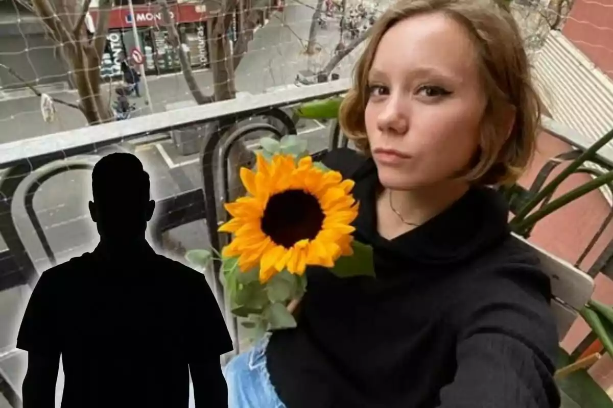 Una persona sostiene un girasol mientras está sentada en un balcón con vista a la calle.