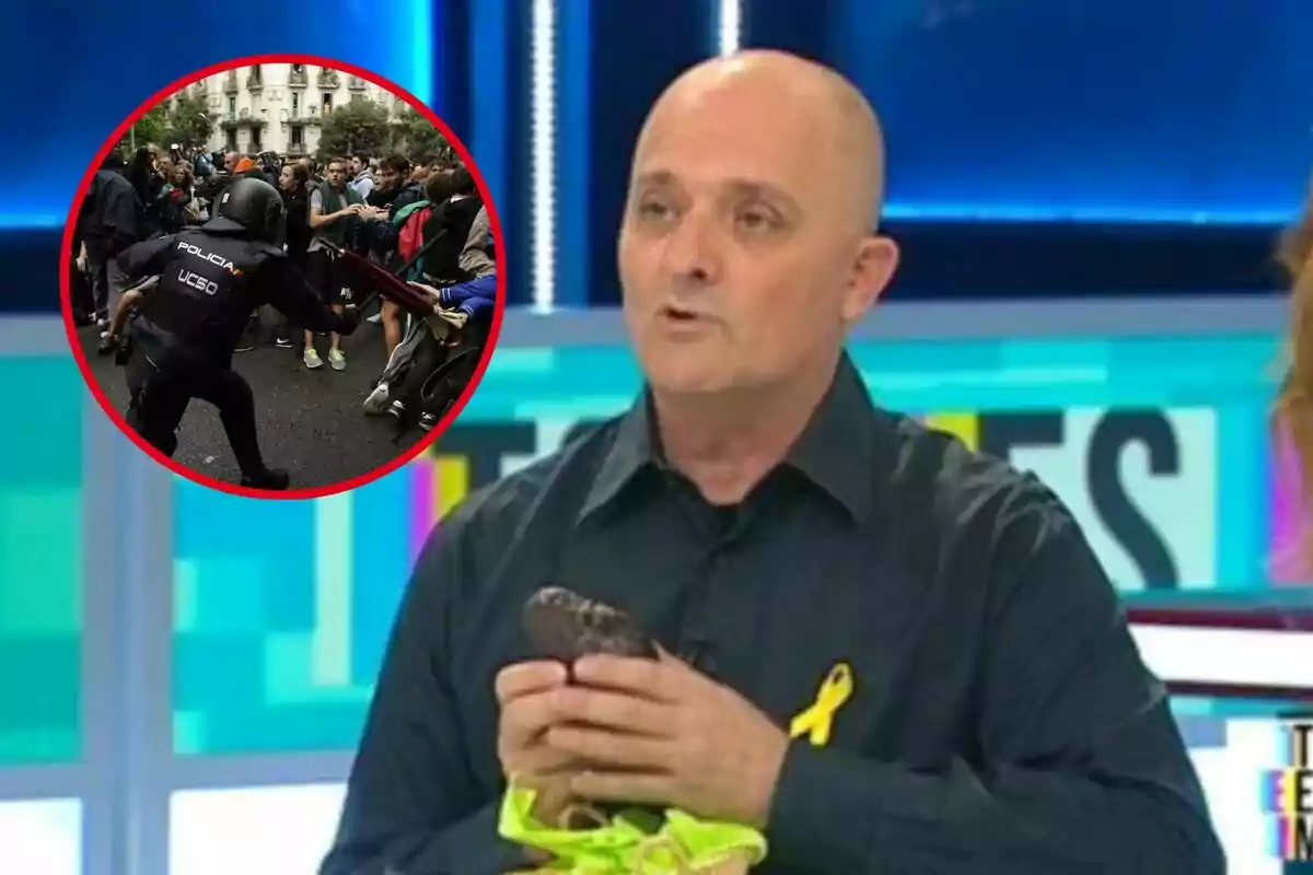 Un home amb una camisa fosca i un llaç groc sosté un objecte mentre parla en un programa de televisió; en un requadre es mostra una escena d?un enfrontament entre un policia i manifestants.