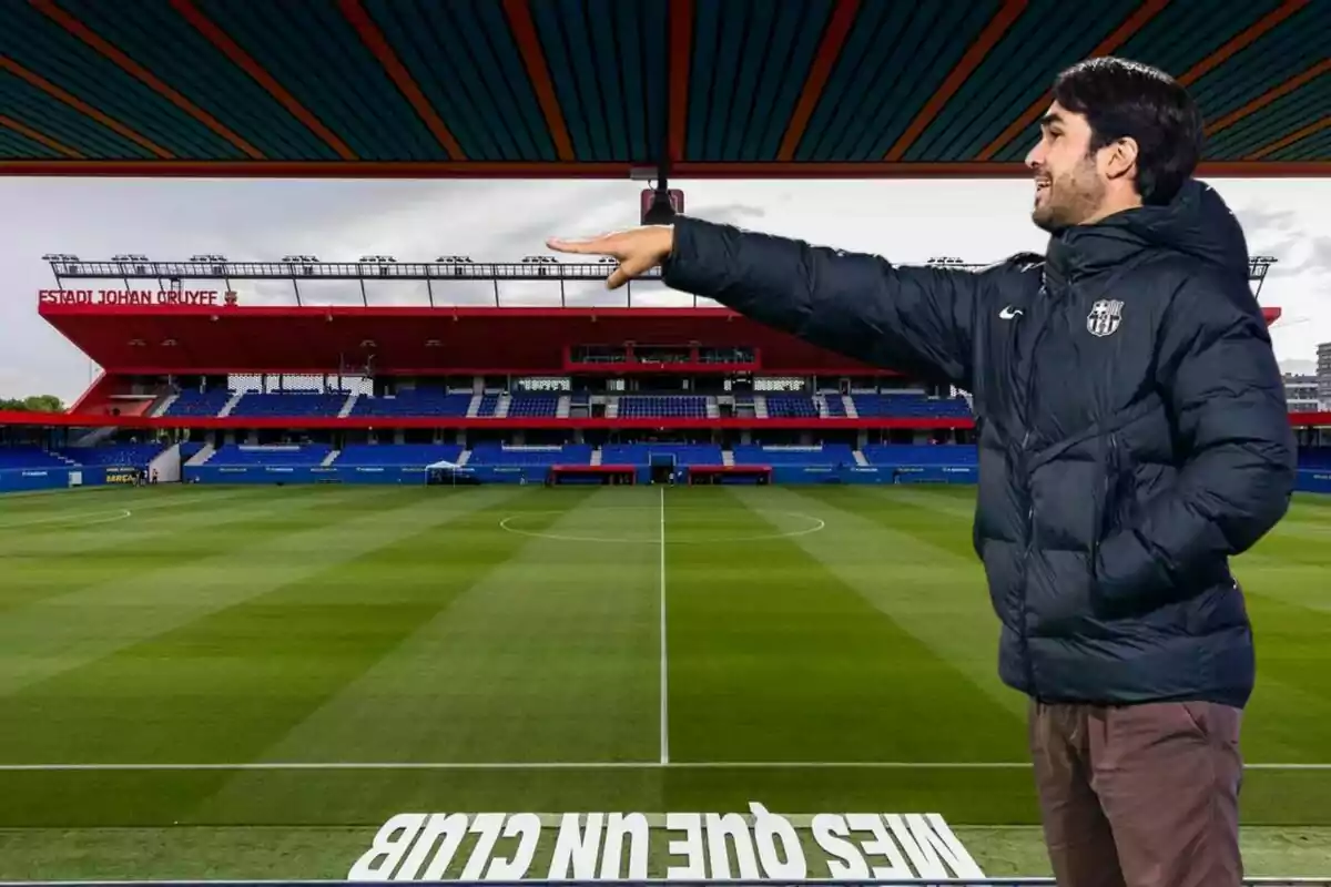 Un home amb jaqueta fosca està dret en un estadi de futbol buit, assenyalant cap al camp.