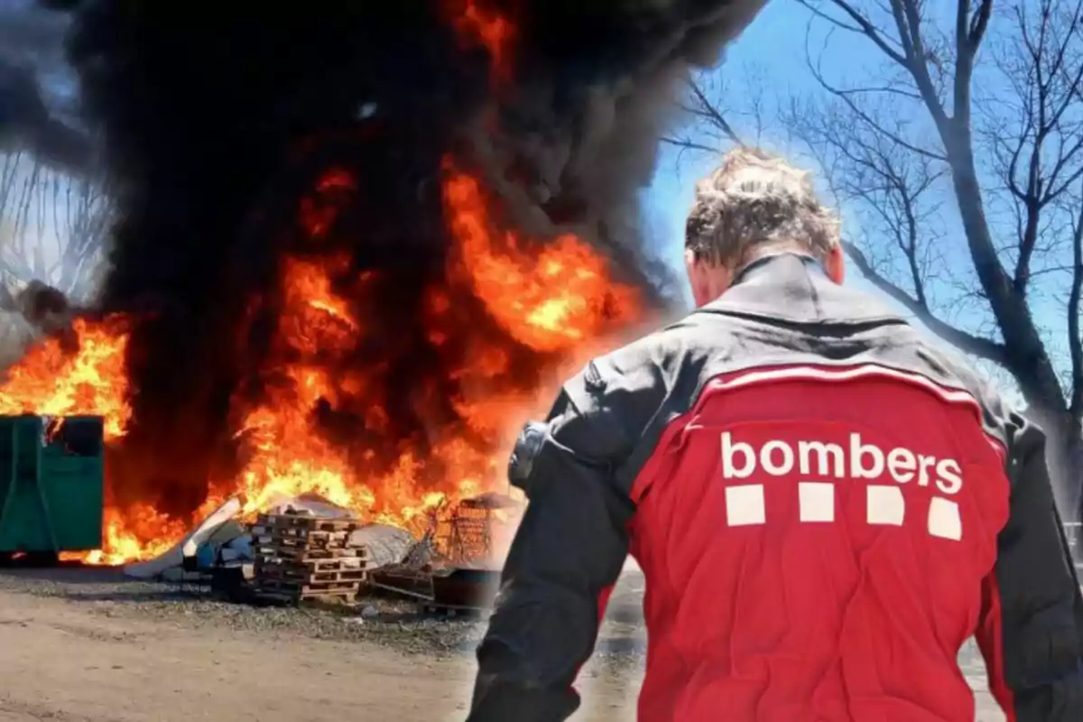 Un bomber d?esquena observa un incendi amb grans flames i fum negre en una àrea al?aire lliure.