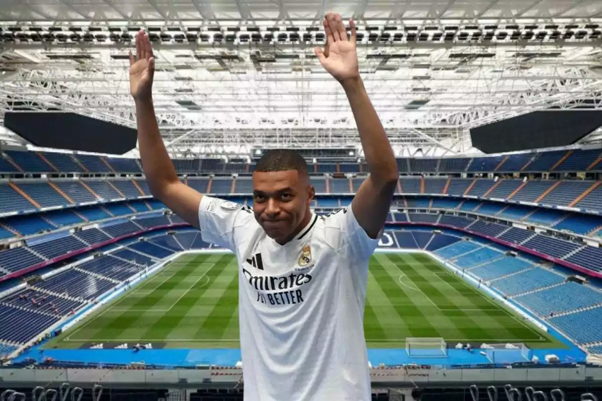 Un jugador de fútbol con uniforme blanco levanta los brazos en un estadio vacío.