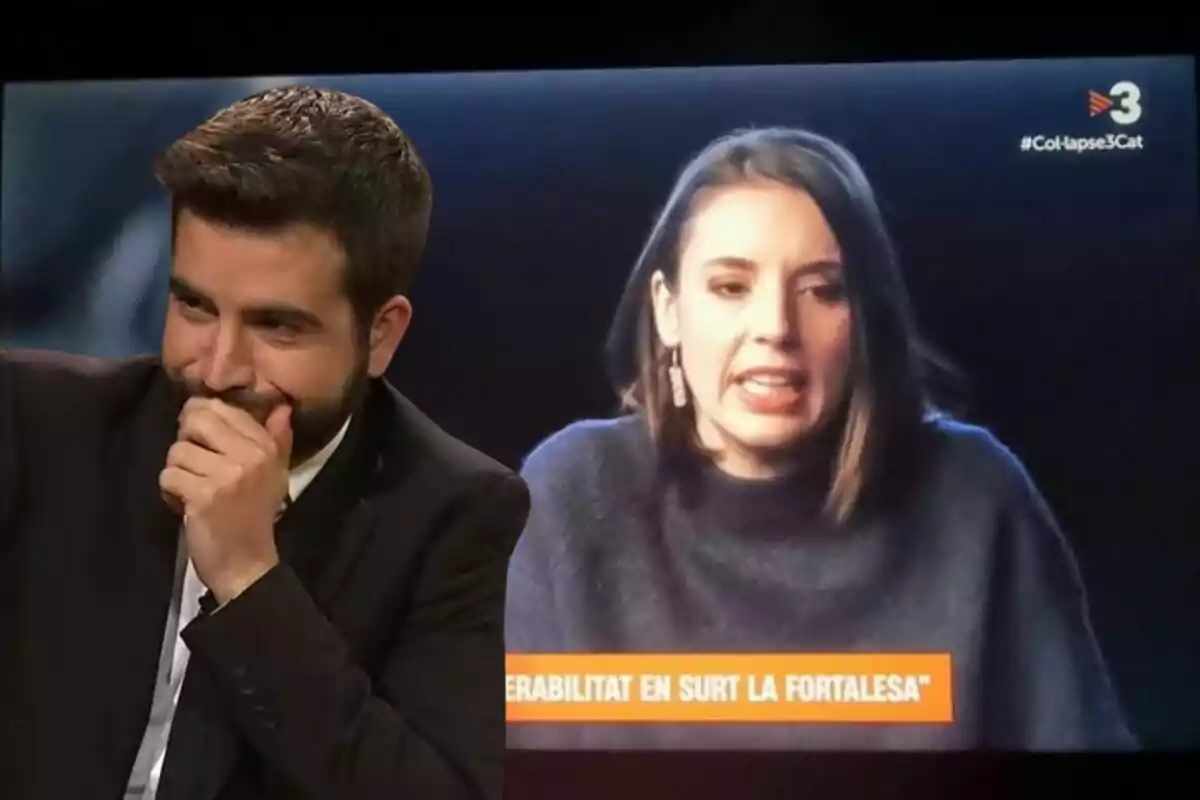 Un home somrient amb la mà a la boca està assegut davant d'una pantalla que mostra una dona parlant en un programa de televisió.