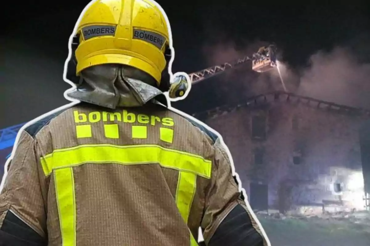 Un bomber amb uniforme groc i casc observa un edifici en flames mentre una escala de bombers ruixa aigua sobre el foc.