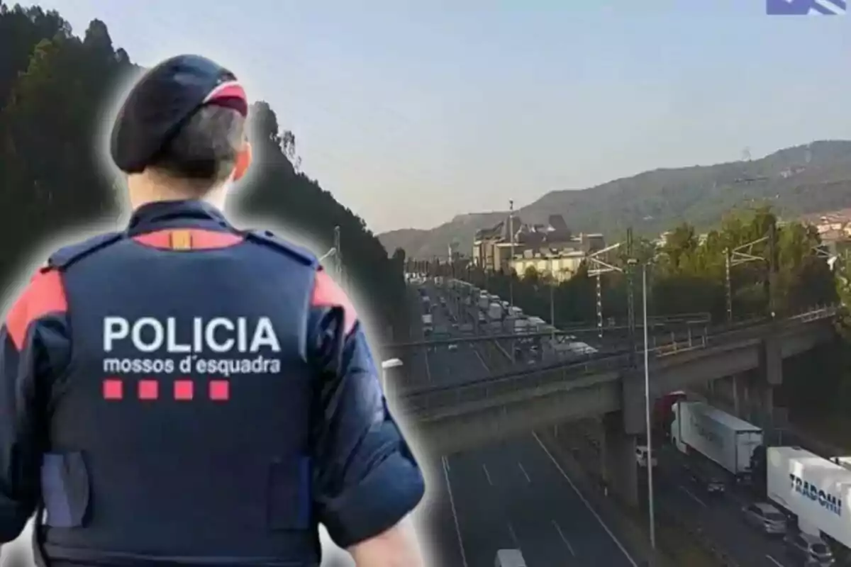 Un agente de los Mossos d'Esquadra de espaldas observa una autopista con tráfico denso y camiones en un entorno de montaña
