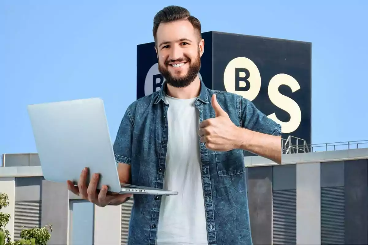 Hombre sonriente con barba sosteniendo una laptop y haciendo un gesto de aprobación con el pulgar hacia arriba frente a un edificio con un cartel que tiene las letras B y S. Hombre sonriente con barba sosteniendo una laptop y haciendo un gesto de aprobación con el pulgar hacia arriba frente a un edificio con un cartel que tiene las letras B y S.