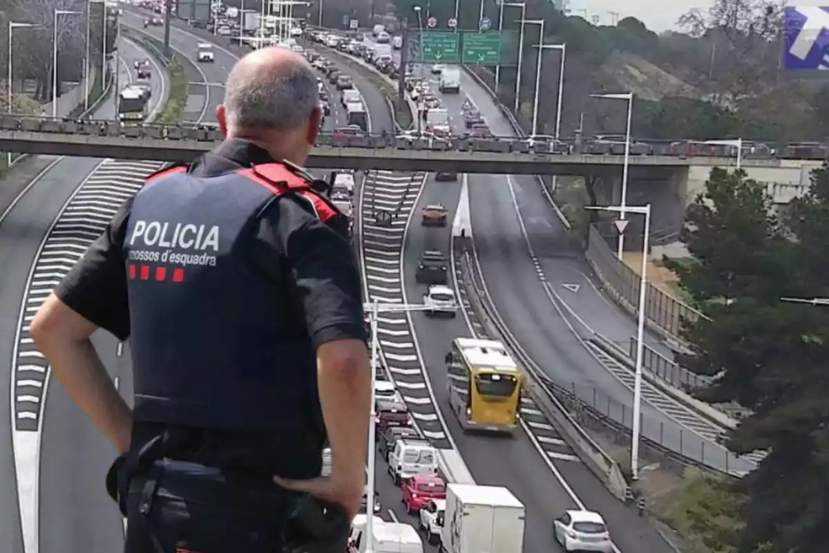 Un agente de policía observa el tráfico en una autopista desde un puente mientras los vehículos avanzan en ambas direcciones.