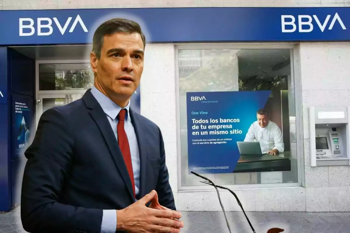 Un hombre de traje frente a una sucursal del BBVA con un cartel publicitario en la ventana.