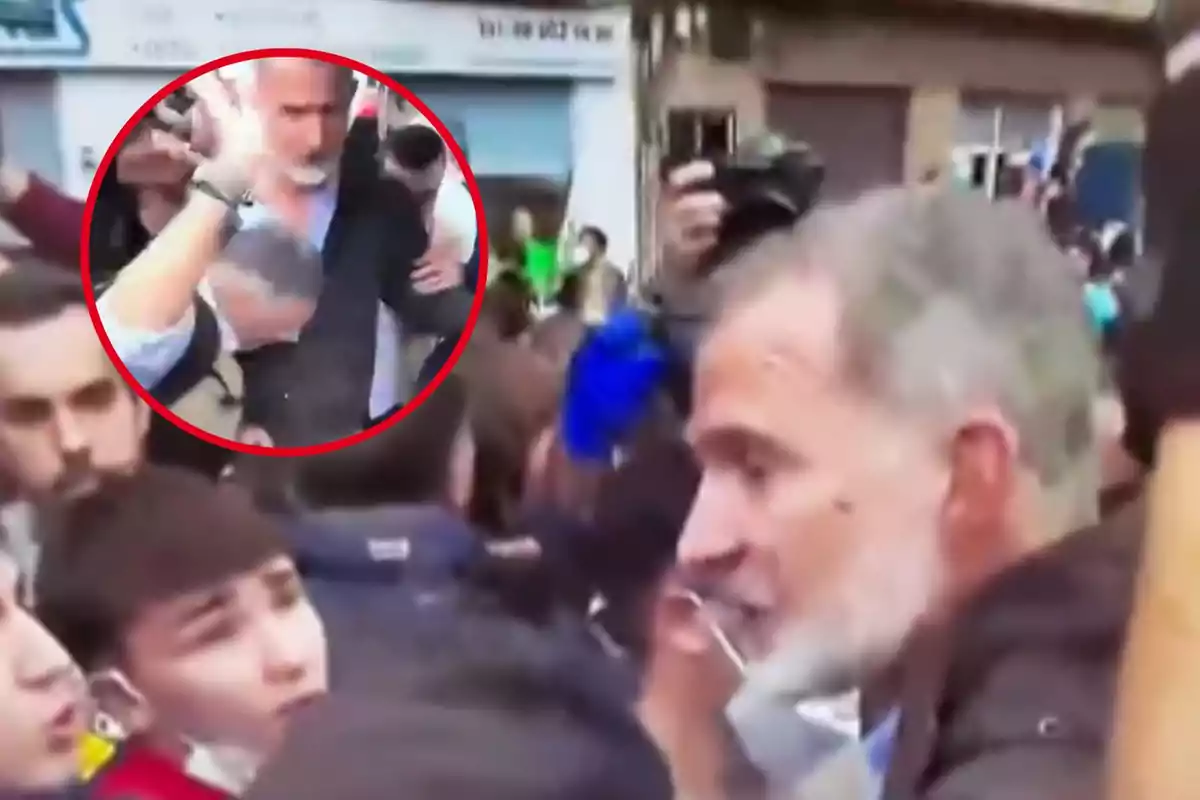 Un hombre de cabello canoso se encuentra en medio de una multitud mientras es rodeado por personas y cámaras.