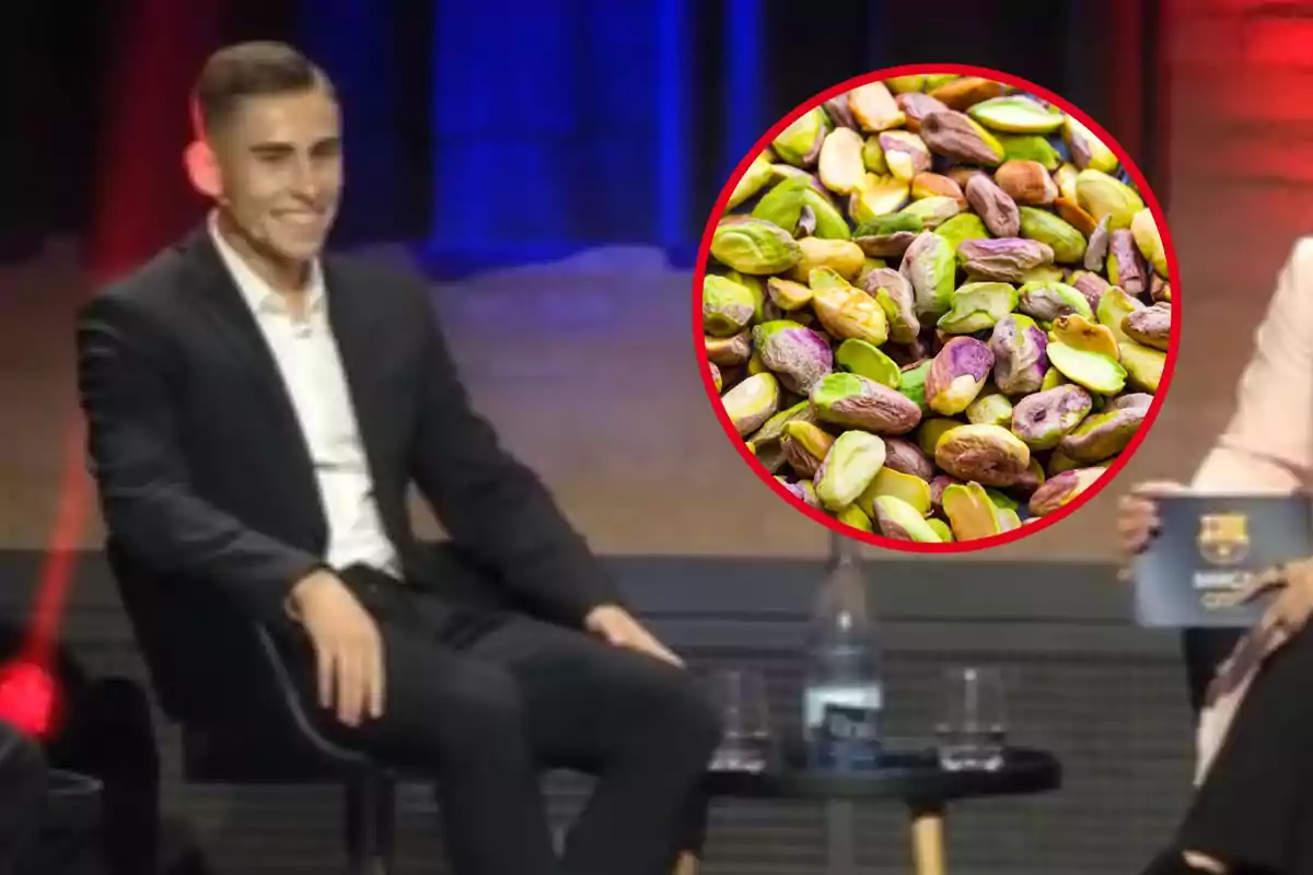 Un hombre sonriente sentado en un escenario junto a una mesa con una botella de agua y un círculo que muestra una imagen de pistachos.