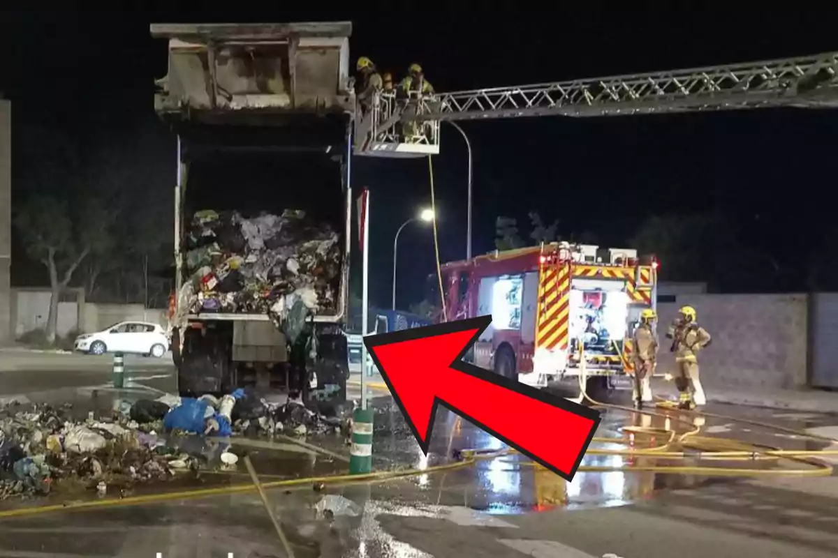 Un camió d'escombraries ha buidat el seu contingut al carrer mentre els bombers treballen a l'escena amb una escala i un camió de bombers il·luminat.