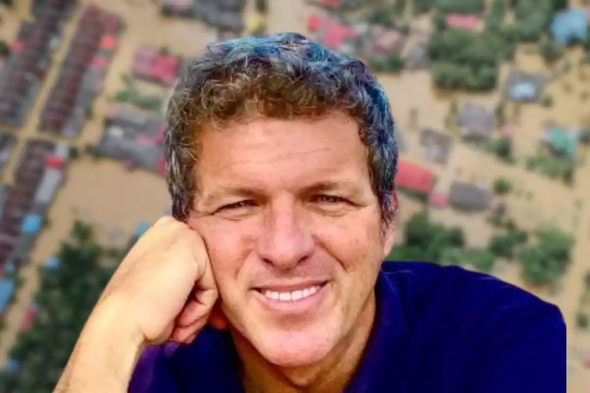 Un hombre sonriente con el fondo de una vista aérea de una zona inundada.