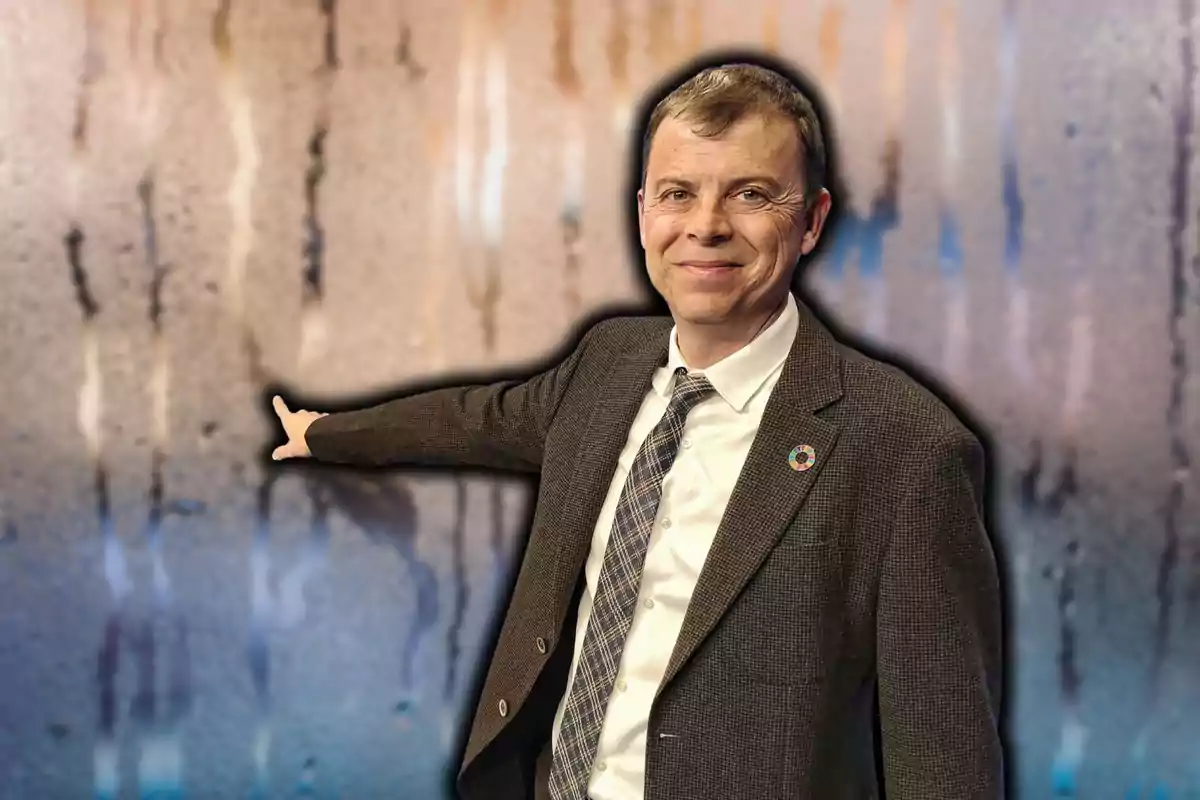 Un hombre sonriente con traje y corbata señala hacia un fondo abstracto con colores difuminados.