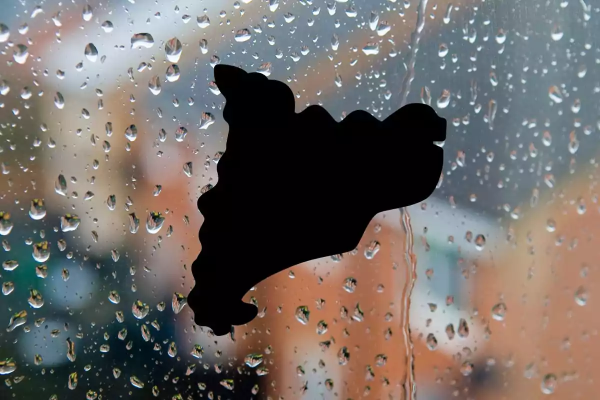 Una silueta negra en forma de mapa sobre una ventana con gotas de lluvia.