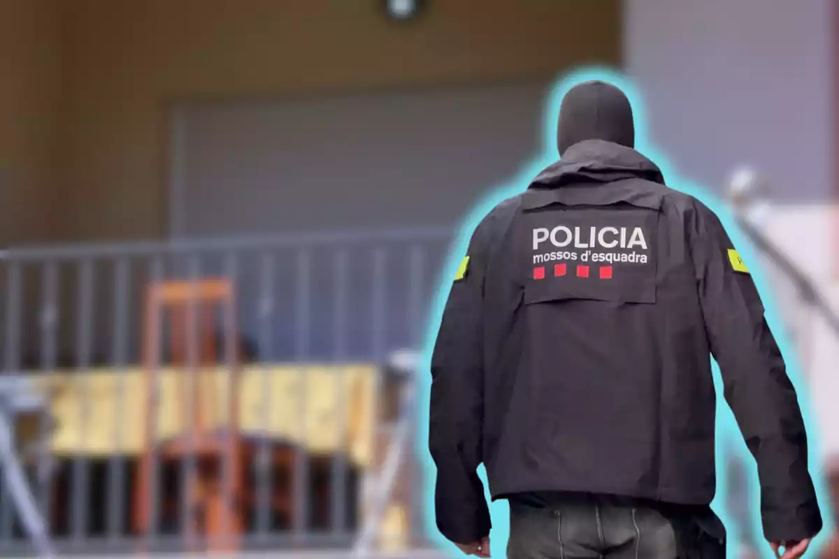 Un agente de policía de espaldas con una chaqueta que dice "Policía Mossos d'Esquadra" frente a un edificio.