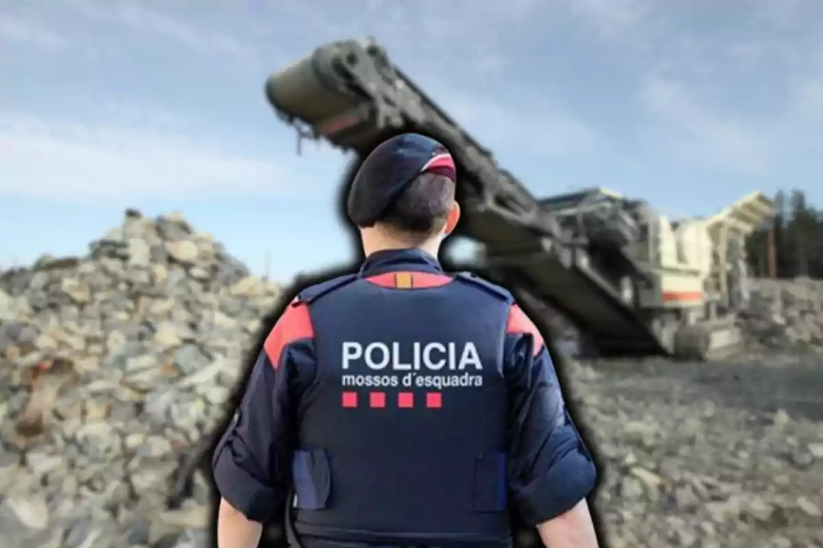 Un agente de policía de espaldas con uniforme de los Mossos d'Esquadra en un sitio de construcción con maquinaria y escombros.