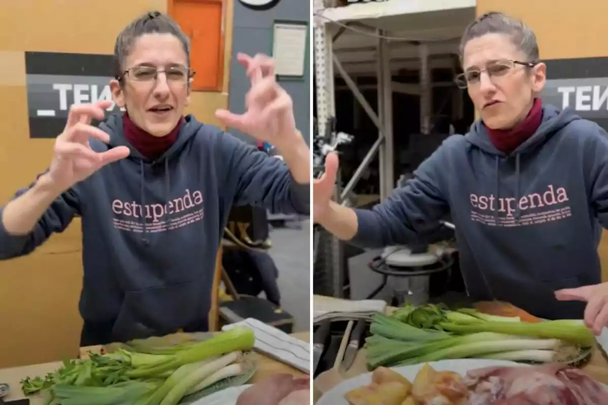 Una persona con gafas y sudadera que dice "estupenda" gesticula con las manos frente a una mesa con verduras y otros ingredientes en un entorno de cocina.