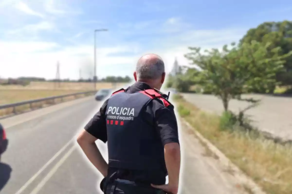 Un agent de policia d?esquena en una carretera rural sota un cel clar.