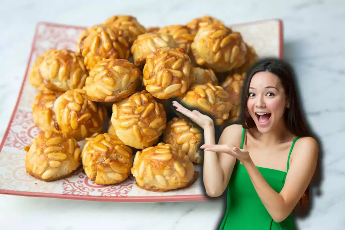 Una mujer sonriente con un vestido verde señala un plato lleno de panellets decorados con piñones.